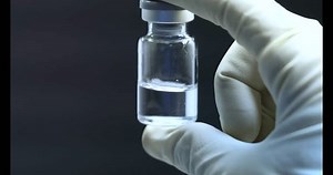 visual inspection of vaccine vials injection vial liquid medicine drug. a hand holding a vial glass bottle in front of light board with gloves on hands to check for impurities in production factory
