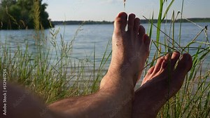 Bare feet of a man in nature near the river. Relaxation, peace and solitude of man with nature. Beach, summer, tan, men's feet.
