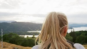 A young blonde woman standing at the summit the view during a mountain hike, close up, back view