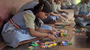 Indian Village school girls or students wearing uniforms sitting together indoors busy playing with colorful blocks as part of a group learning activity, Kudal, Maharashtra, India (March 2022)