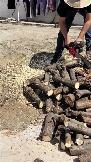 Cutting small wood logs into many pieces using a handheld electric chainsaw in an outdoor area