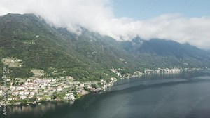 Drone footage panning across the shores of Lake Como in Italy. Clouds over the mountains and famous villas along the shoreline can be seen.