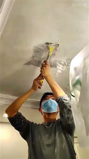Scraping damaged ceiling texture using metal putty knife and applying fresh plaster to create smooth