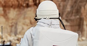 Rear of the spaceman in the white space costume with head armor walking the Mars or other unhabited planet. Back view. Close up. Outdoors.