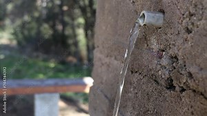 Pure mineral water flowing from a spout of a stone fountain in the forest