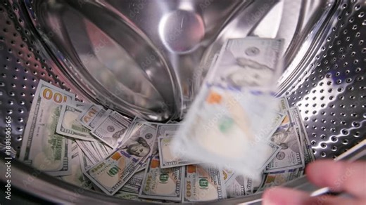 hand is adding the US Dollar banknotes inside a washing machine drum, money laundering and fraud concept.