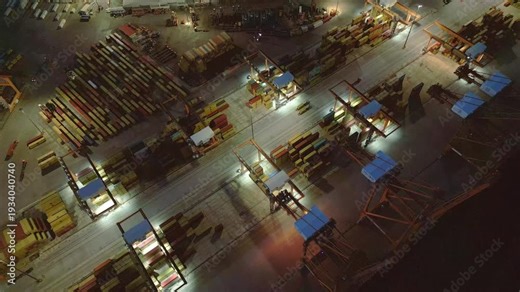 Aerial drone footage showing general container terminal activity at a busy industrial cargo port during evening hours. Stacked shipping containers, cranes and freight logistics infrastructure
