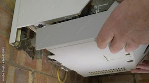 Closeup POV shot of a man’s hands removing the lower metal cover of an old traditional, wall mounted, domestic gas boiler, ready to service / repair.