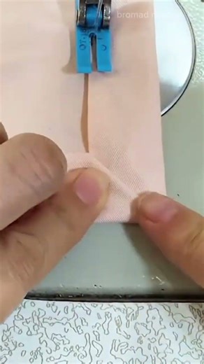 sewing a peach fabric with a neat stitch pattern using a white electric sewing machine at workspace