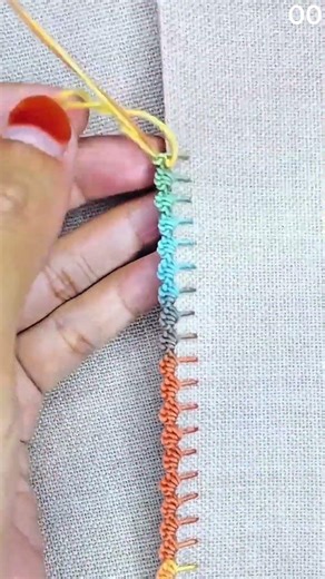 Needle guided with yellow thread stitches colorful edge pattern on fabric border