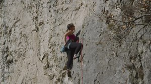 Sporty lady climbing a difficult route in steep rock face on sunny Karst Edge. She is using chalk for a better grip and continues to climb. An outdoor adrenaline sports activity in vertical landscape.