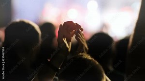 Young person clapping in concert of popular foreign rock band. Crowd of fans enjoying moment. Lights, without faces. Outdoors, music, evening.