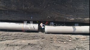 Concrete pipe tube installation. Aerial above men at work outside with heavy machinery to connect and install water or sewerage pipeline in a digging soil land