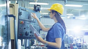 Professional Female Operator in Hard Hat Setting up/ Programming CNC Machine with Control Panel in a Big Industrial Factory. Shot on RED EPIC-W 8K Helium Cinema Camera.