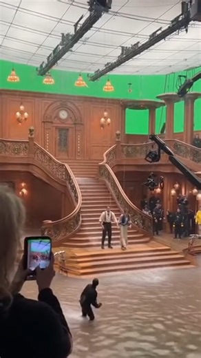 studiobrakdown on Instagram: "Titanic BTS: How the Grand Staircase Reunion Scene Was Filmed 🚢🎬 Step behind the camera and see how Titanic ka iconic Grand Staircase moment actually shoot ho raha hai. Massive indoor set par full wooden staircase, balcony rails, wall lamps, and clock detail perfectly recreated hai, peeche giant green screen walls visible hain. Upar se grid-style ceiling rig me hanging lights aur camera rails lage hue, crew in black clothing sides me lineup ho kar scene prepare ka