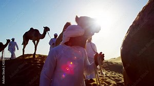 Arab Bedouin males in traditional dress leading camels through hot desert