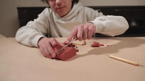 clip-3999440293-young-person-delicately-slicing-red-modeling-clay