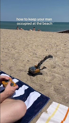 Guy is playing with a remote-controlled excavator at the beach!