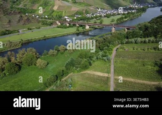 Aerial drone footage of a sweeping panoramic view over the Moselle river valley in Rhineland-Palatinate, Germany, near the Geierlay area. The footage reveals a red railway bridge crossing the Moselle, a traditional wine village with a church tower o Stock Video Footage - Alamy