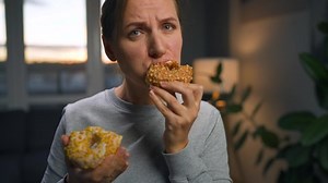 Binge eating concept. Caucasian woman with eating disorder eating two donuts quickly and at the same time.