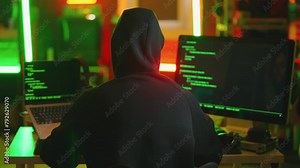 Hacker writing code cracking computer. Man programmer in hoodie cracks system, using computer in dark room back view. Hacker attack, technology, virus infected software, programmer man concept.