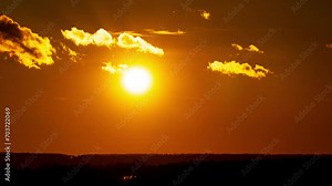 Bright orange sunset behind the departing clouds. The sun goes below the horizon at the end of the day. Sunset with shining sun descending through layers of clouds time lapse.