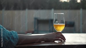 unrecognizable girl hand takes a glass of beer against the backdrop of a country house backyard. lonely woman drinks beer in backyard.