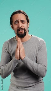 Vertical video Man putting hands together in apology gesture, asking for forgiveness. Apologetic person doing sorry gesturing, asking for pardon, isolated over studio background, camera B