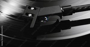 Extreme closeup of turntable's tonearm headshell lowering on spinning vinyl record