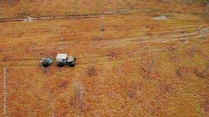 Shot on a drone. The all-terrain vehicle slowly drives through the swamp on a broken road. A swamp walker ride with a trailer off-road.