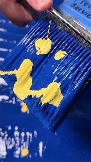 applying yellow paint over the blue surface using a metal comb for creating unique artistic texture