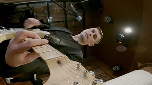 Male guitarist singing on microphone while playing guitar on stage. Young performer performing at event. He is wearing black formals. Vertical video