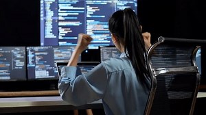 Back View Of Asian Female Programmer Celebrating Succeed Writing Code By A Laptop Using Multiple Monitors Showing Database On Terminal Window Desktops In The Office