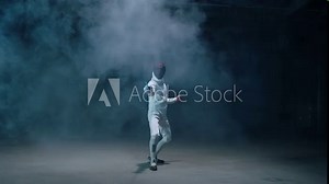 Professional fencer in protective uniform practicing maneuvers with sword alone in dark studio . Fencing demonstration on black smoked background . Shot on Arri Alexa cinema camera in slow motion .