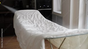 Professional janitor male cleaning white blanket with hot wet steam using electric steam cleaner in living room. Concept of maintenance modern home appliance. Shooting in slow motion.