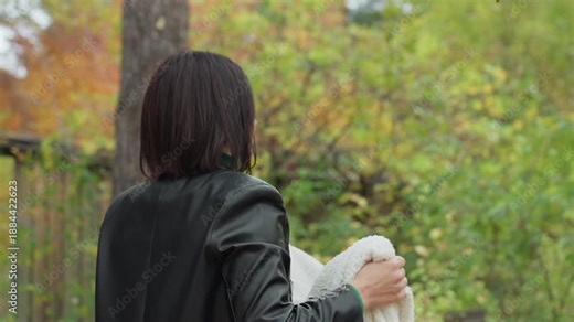 woman in leather jacket unfolding blanket amid autumn forest, draping cozy white throw over branch gentle deliberate movements captured from profile and back moody overcast light, dense foliage