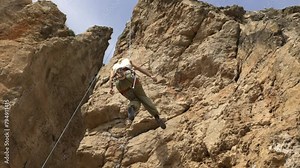 Adult female rock climber descends from a cliff on a rope - rock climbing