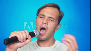 a crazy funny young man sings songs into a microphone. color background, close-up. 4k, slow motion