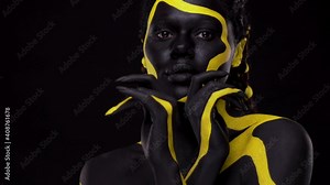 Face art. Dancing woman with black and yellow body paint. Young african girl with colorful bodypaint. An amazing afro american model with yellow makeup. Closeup face.