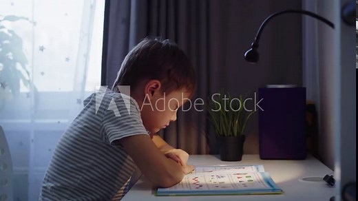Little boy doing homework at home. kid reading a book at the table by the light of lamp. High quality FullHD footage