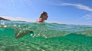 Girl swimmer in green swimsuit underwater at sea. Young woman dives and swims in clear sea water. Half underwater slow-motion shot, Active healthy fitness lifestyle