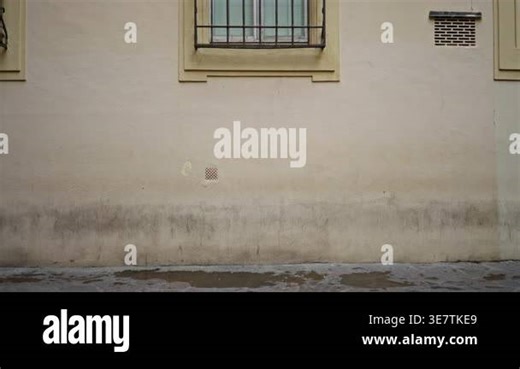 Beige plaster wall texture with window bars, small vent and damp lower band, sharp detail on urban street background; background backplate copyspace calm Stock Video Footage - Alamy