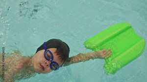 kids training class in swimming pool swim lesson for 5 year old child training to swim holding green board moving one hand making swimming movements. swimming class young swimmer sportsman