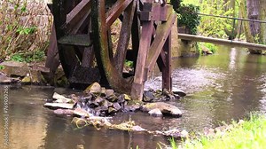 Traditional wooden waterwheel rotating with water flowing in the stream, surrounded by spring greenery and stones. Historical technology in modern times. Peaceful rural atmospheres