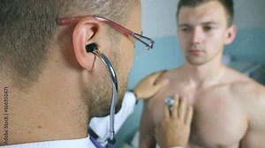 Doctor examining young male patient with stethoscope. Medic checking chest of guy in her office at the hospital. Medical worker listening heartbeat of athletic man. Close up Rear back view