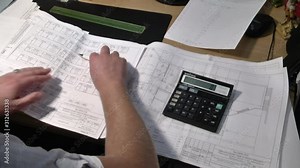 Closeup of human hands drawing architectural plan with pen and calculator. Architect or engineer calculating the plans. Paper electrical engineering drawings.
