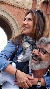 Vertical. Smiling elderly couple having fun together on vacation. Older man piggybacking mature woman enjoying leisure time visiting European city. Concept of people in love relationships in