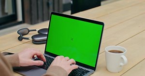 A man is typing on a laptop with a green screen