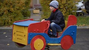 Big boy playing see saw at playground in park at autumn. Kid swinging on the swings in the shape of car on playground in outdoor park