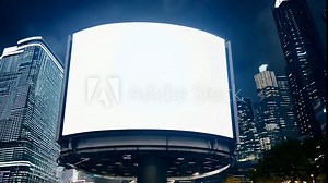A large billboard with a blank white screen is illuminated in a city at night